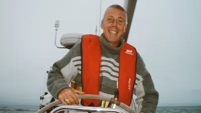 Smiling skipper in an orange life vest at the helm of a yacht – moss-ecommerce