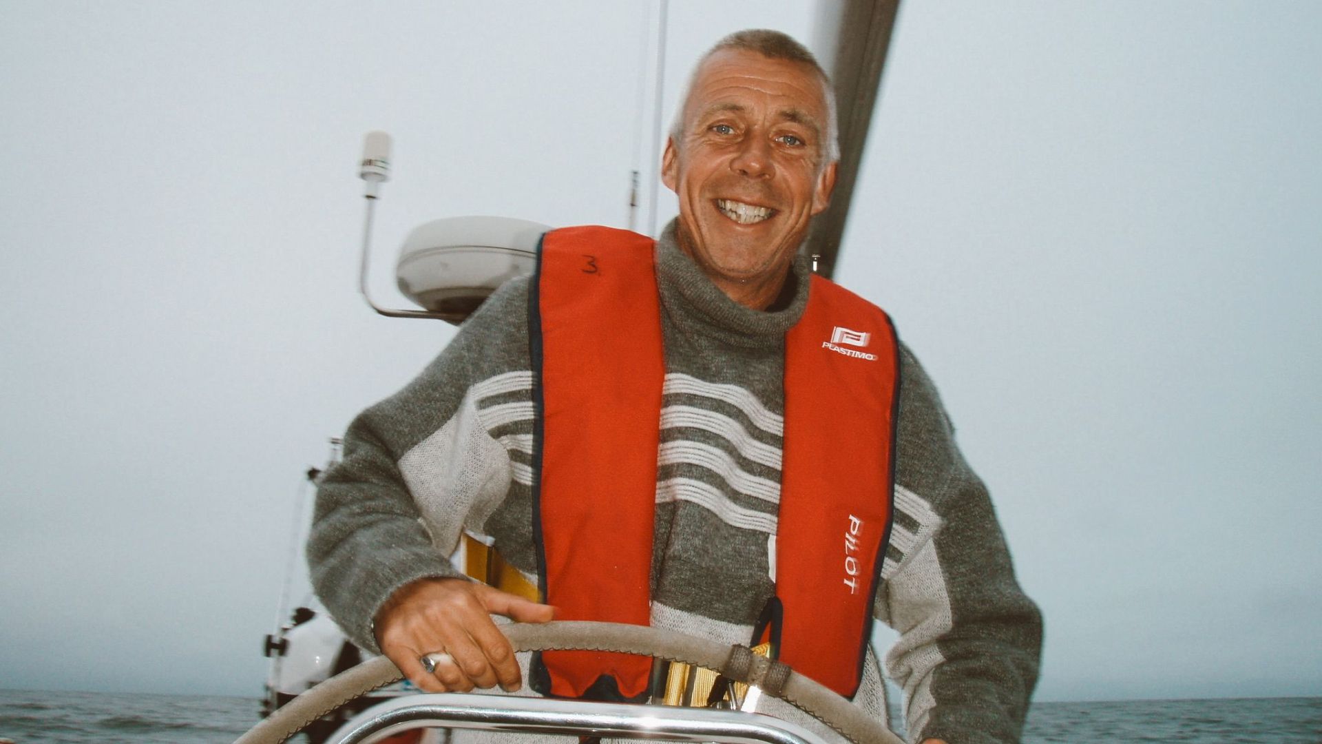 Smiling skipper in an orange life vest at the helm of a yacht