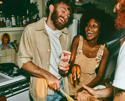 Friends laughing in a kitchen while cooking with Squizzi sauce – squizzi